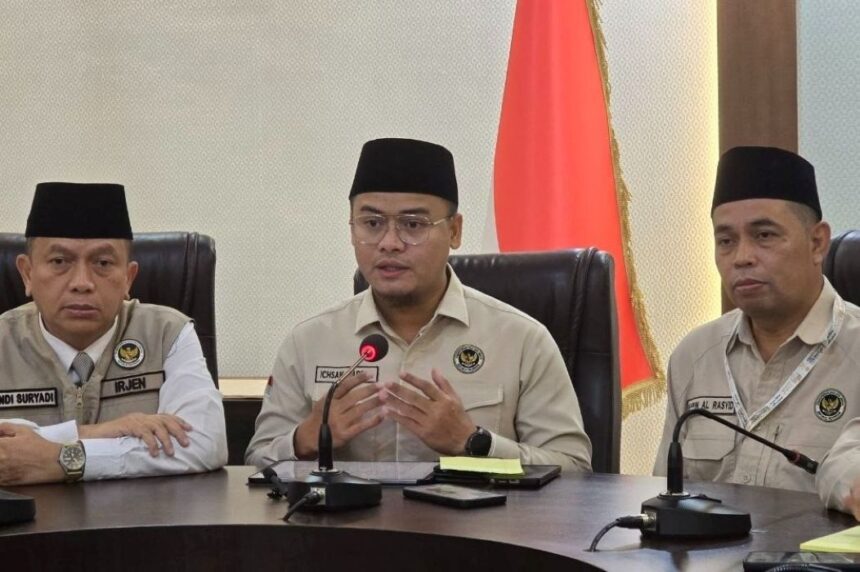 Three men in beige uniforms and black peci hats sit at a conference table during a formal briefing, with an Indonesian flag in the background and microphones in front of them.