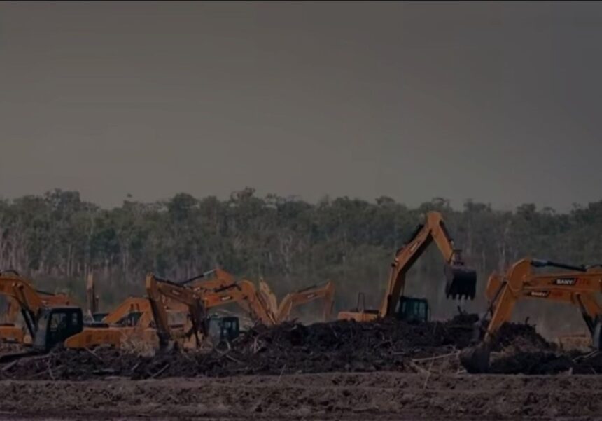 Several orange excavators work on a dirt site with a large pile of debris in the foreground, trees in the background.