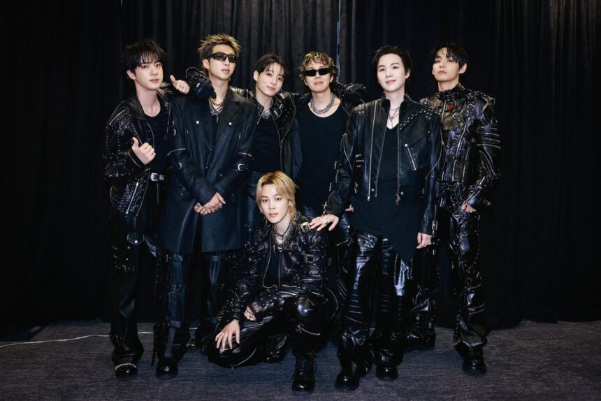 Seven men in black leather outfits posing together backstage against a dark curtain.